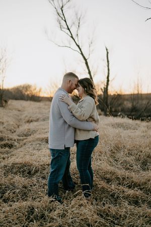 A couple in cozy sweaters shares an intimate moment in a winter field at sunset.