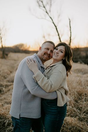 A couple shares a joyful moment together in casual sweaters against a sunset landscape.