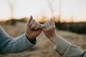 Two people make a pinky promise with an engagement ring visible in the warm evening light.