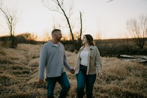 A couple walks hand in hand through a winter field during golden hour.