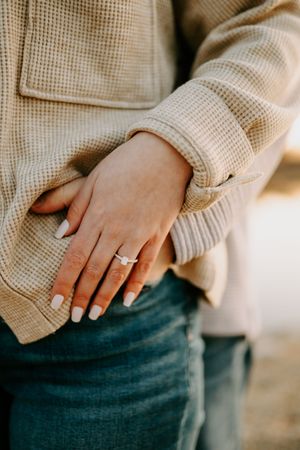 Detail shot of hands with wedding ring against beige sweater texture.