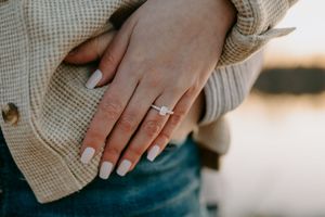 Close-up of hands with engagement ring against cream knit sweater.