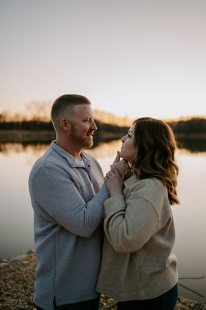 Tender moment between couple against serene lake backdrop at dusk.