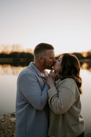 Couple embracing and kissing during golden hour by a waterfront.