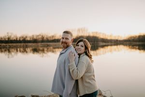 Silhouetted couple embracing by tranquil lake at sunset.