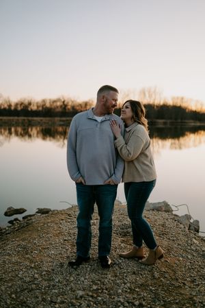 Couple standing on rocky shoreline during sunset photoshoot.