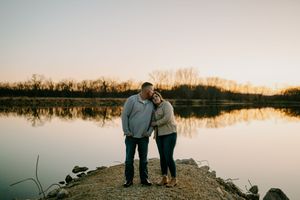 A couple enjoys a quiet moment together on a rocky shoreline during sunset.