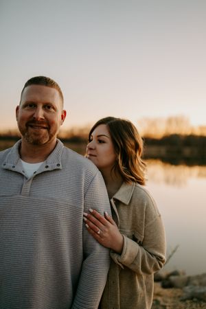 An intimate moment between a couple wearing casual sweaters by a lake at sunset.