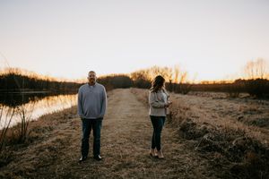 A couple stands together on a natural path during golden hour with water views.
