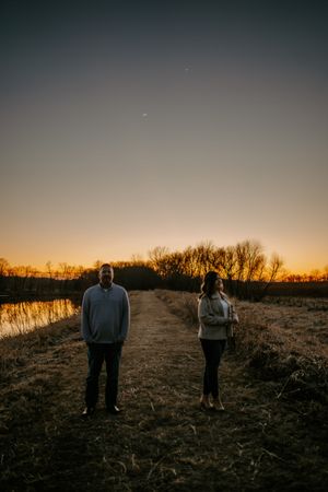 Silhouettes of a couple standing together against a dramatic sunset sky by the water.