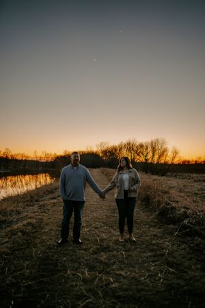 A couple holds hands while walking along a lakeside path during sunset.