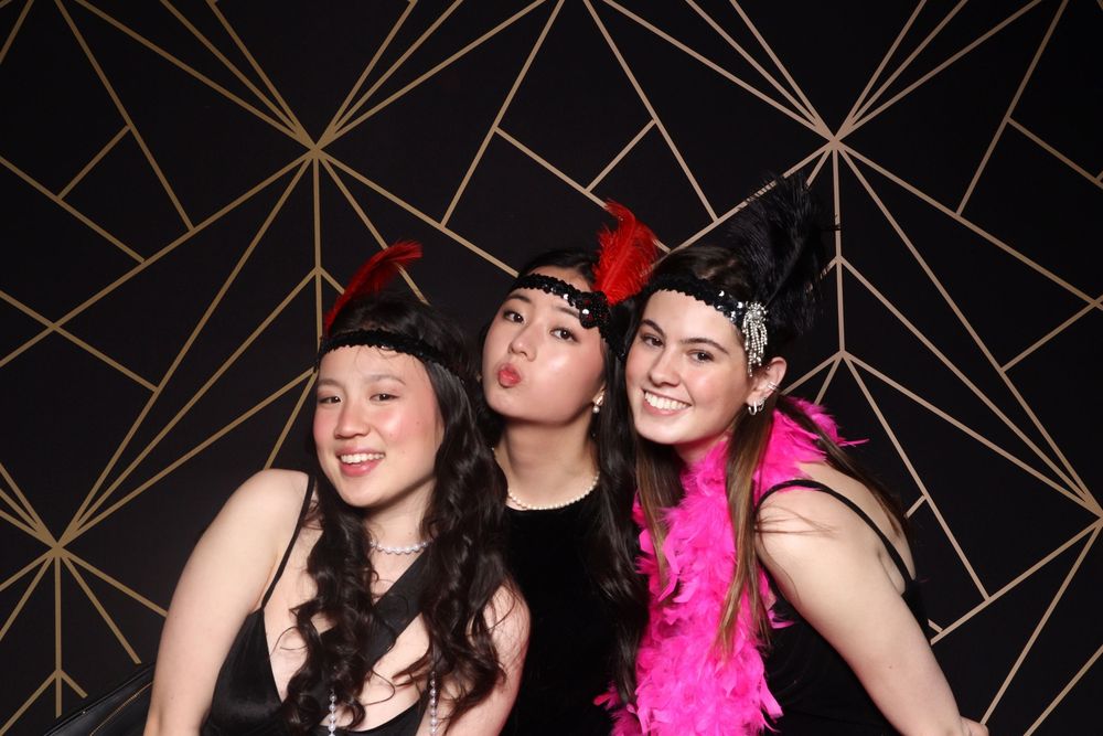A group of individuals pose for a photo booth series wearing festive party accessories including pink feather boas.
