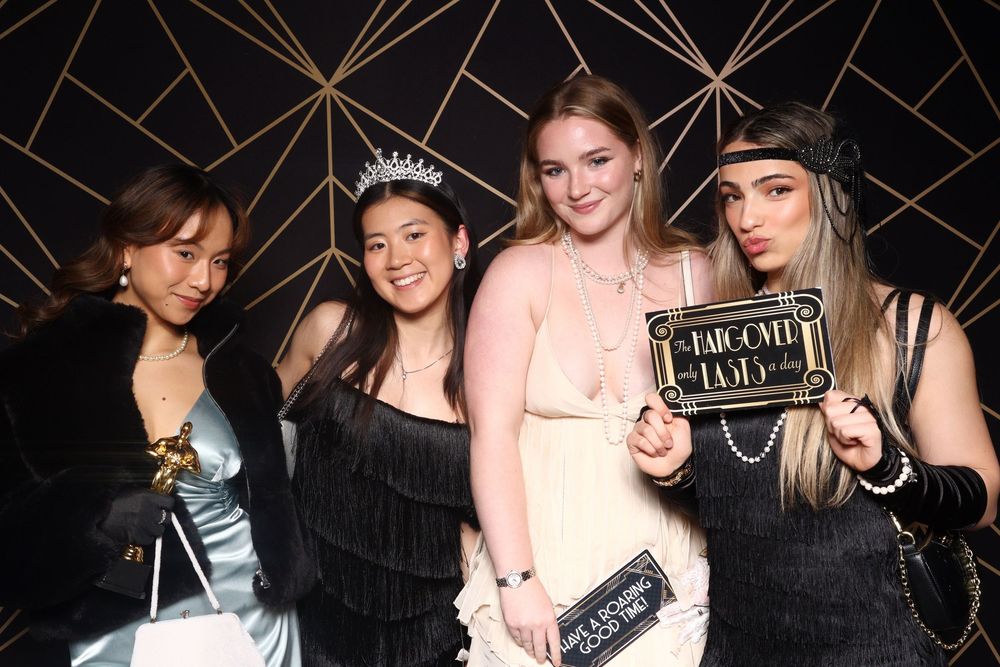 A group of friends pose together at a party with props and a glam backdrop.