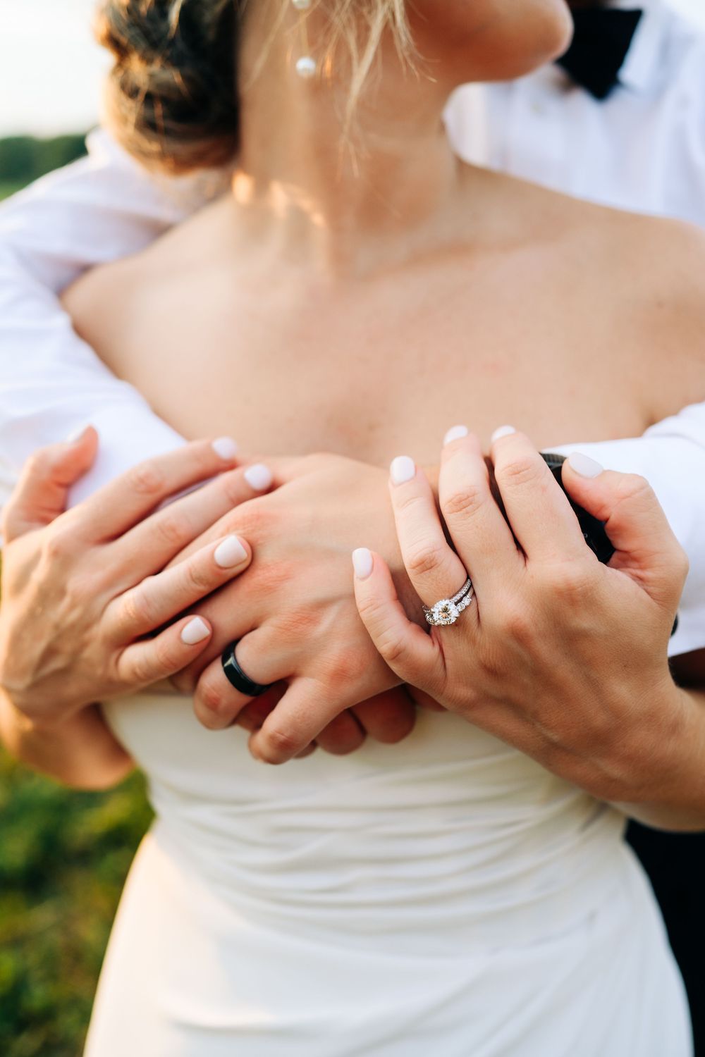 Close-up of hands with wedding rings embracing against a white dress bodice.
