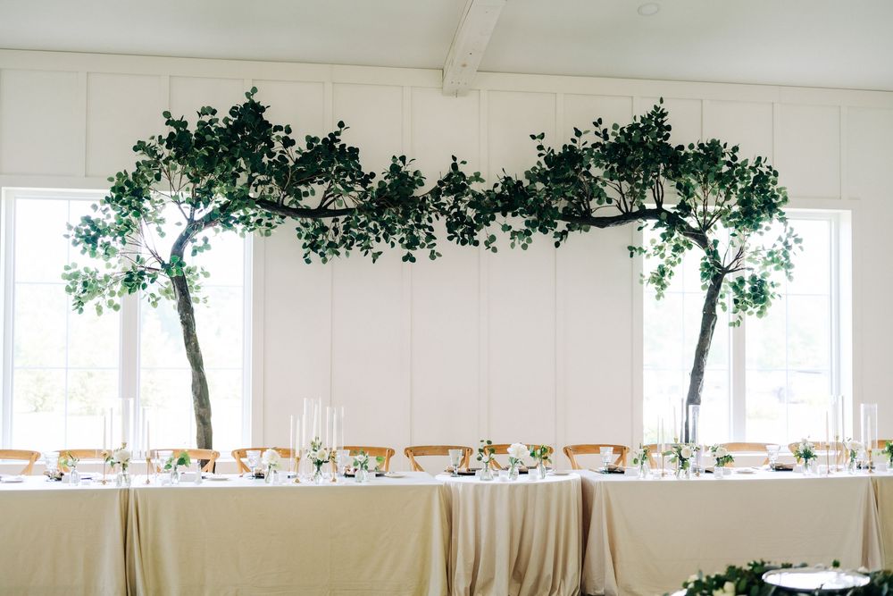 Elegant wedding reception table with greenery arch decoration in a bright white venue.