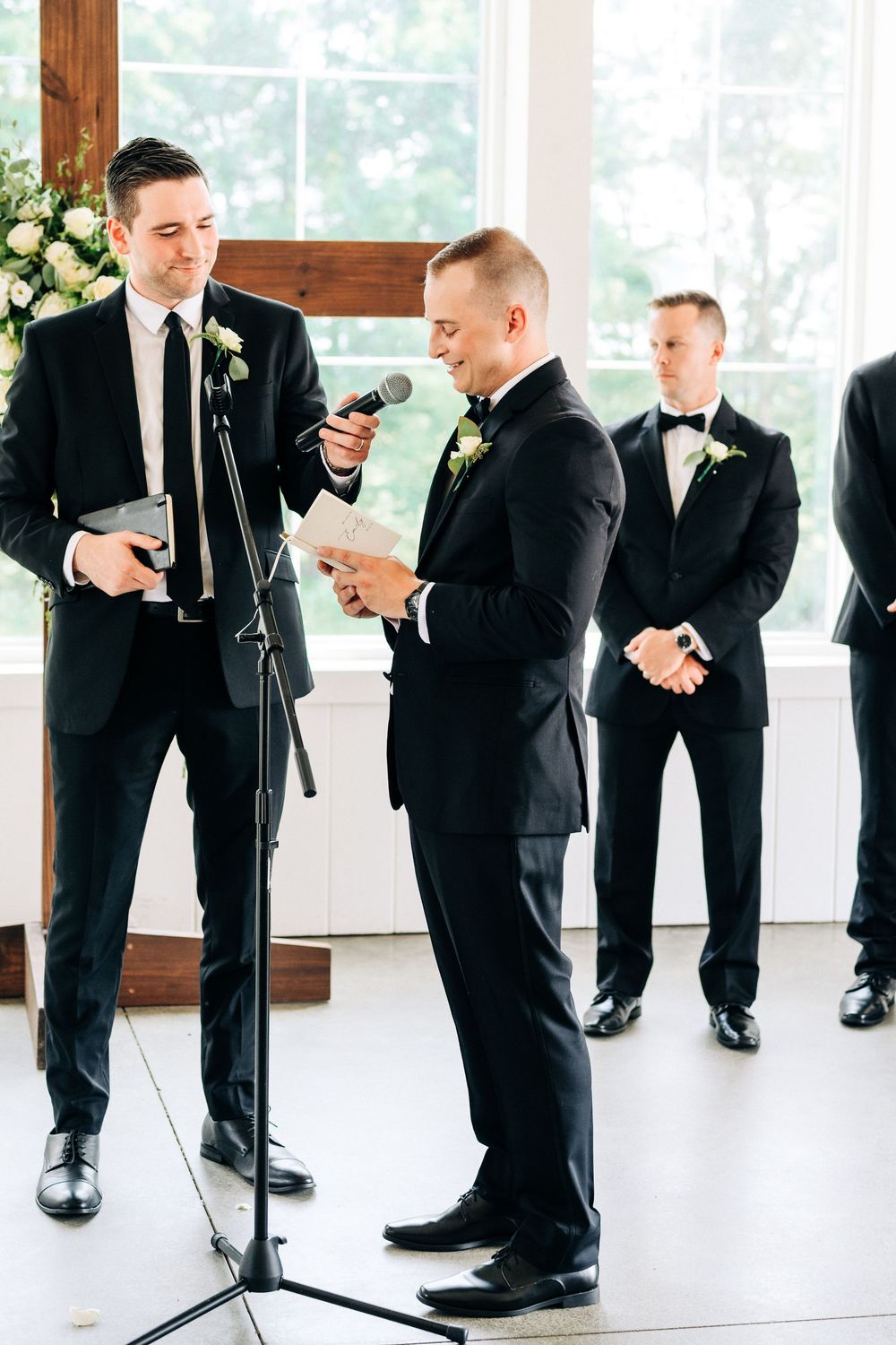 Two groomsmen in black tuxedos exchanging vows at an elegant indoor wedding ceremony.