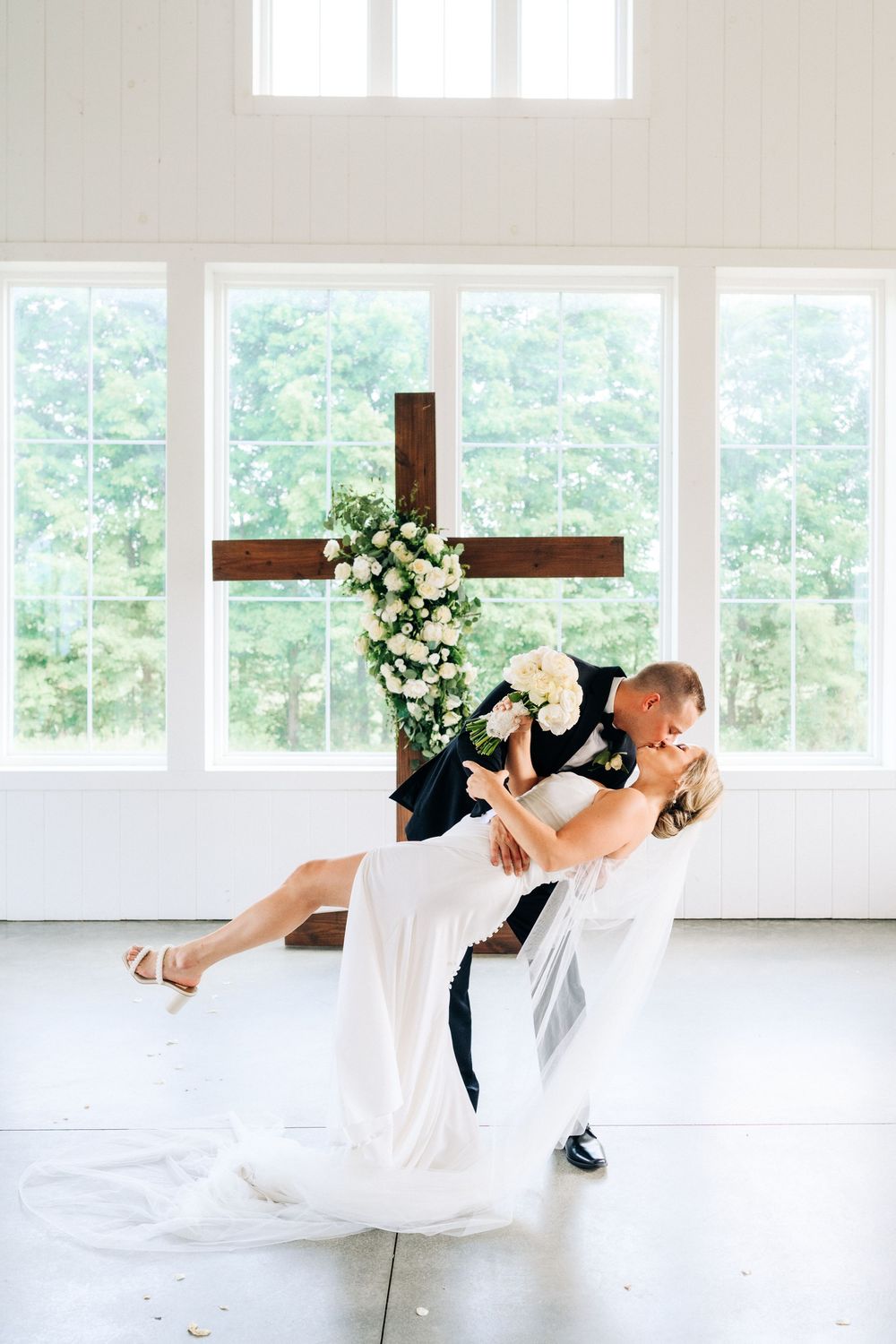A romantic dip pose during first dance with a wooden cross and floral backdrop.