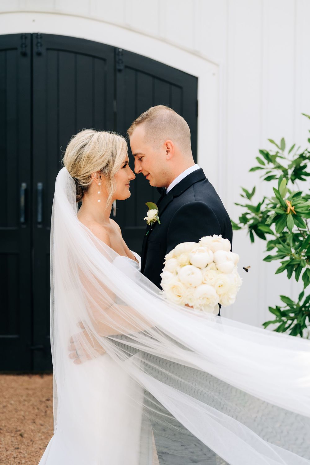 A romantic wedding portrait featuring a bride and groom embracing as her long veil flows in the breeze.