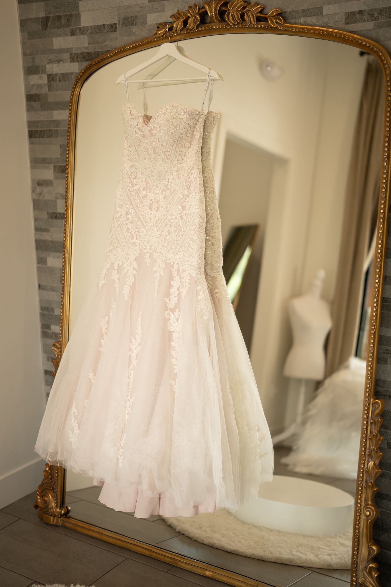 Wedding dress hangs elegantly in front of ornate gold mirror in bridal suite.