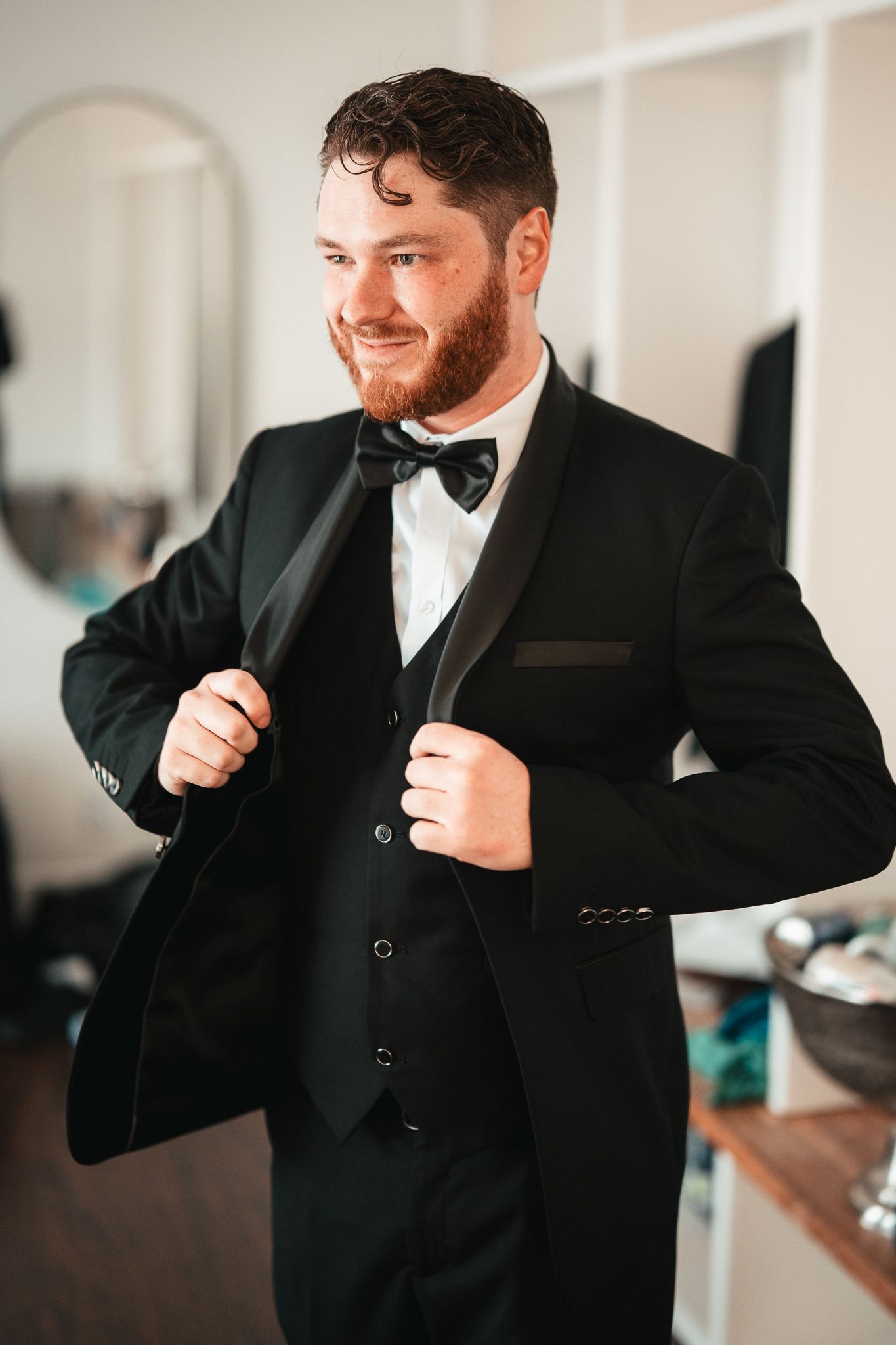 Groom adjusts bow tie while getting ready in formal black tuxedo.