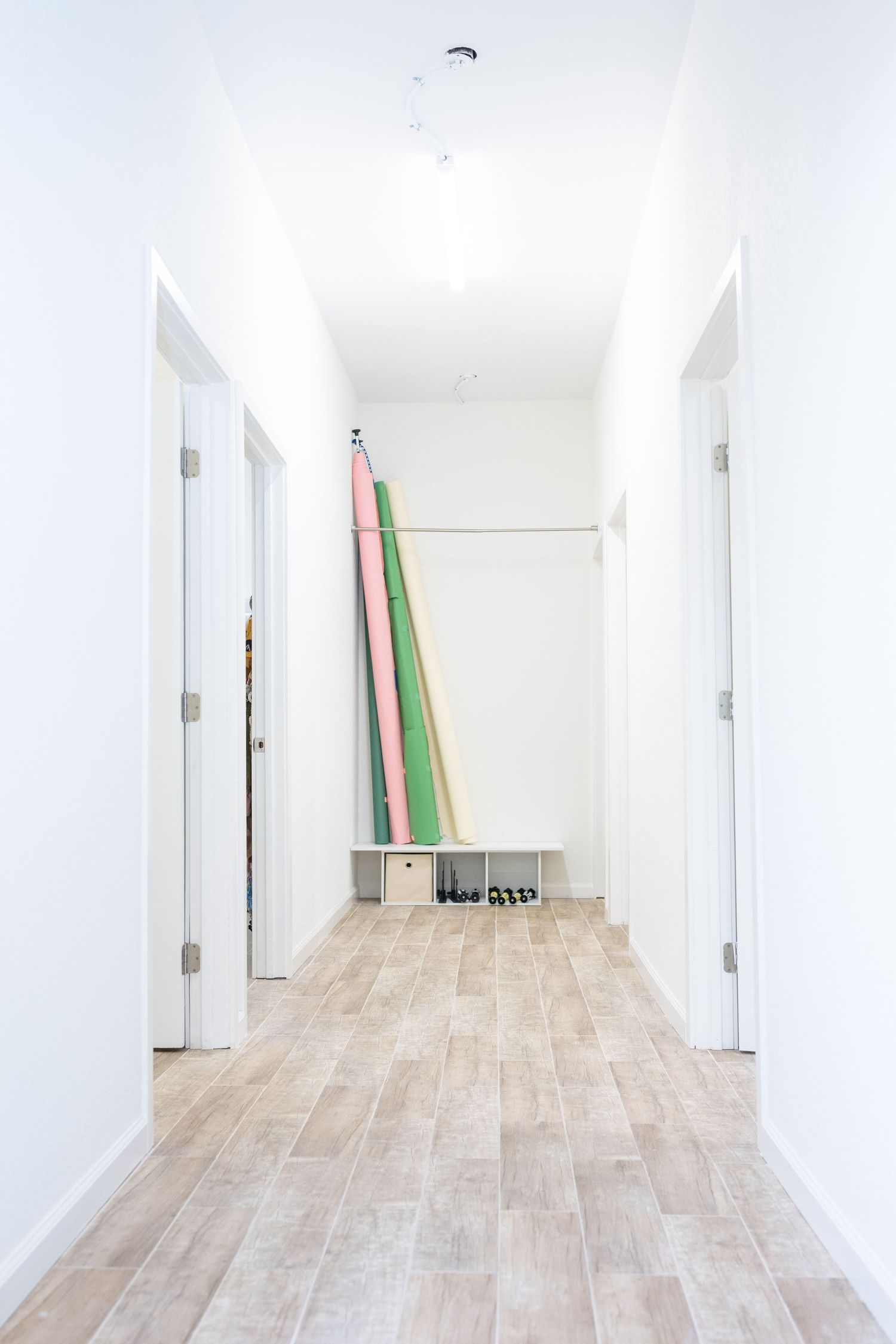 Minimalist white hallway with hardwood floors and surfboards leaning against wall.