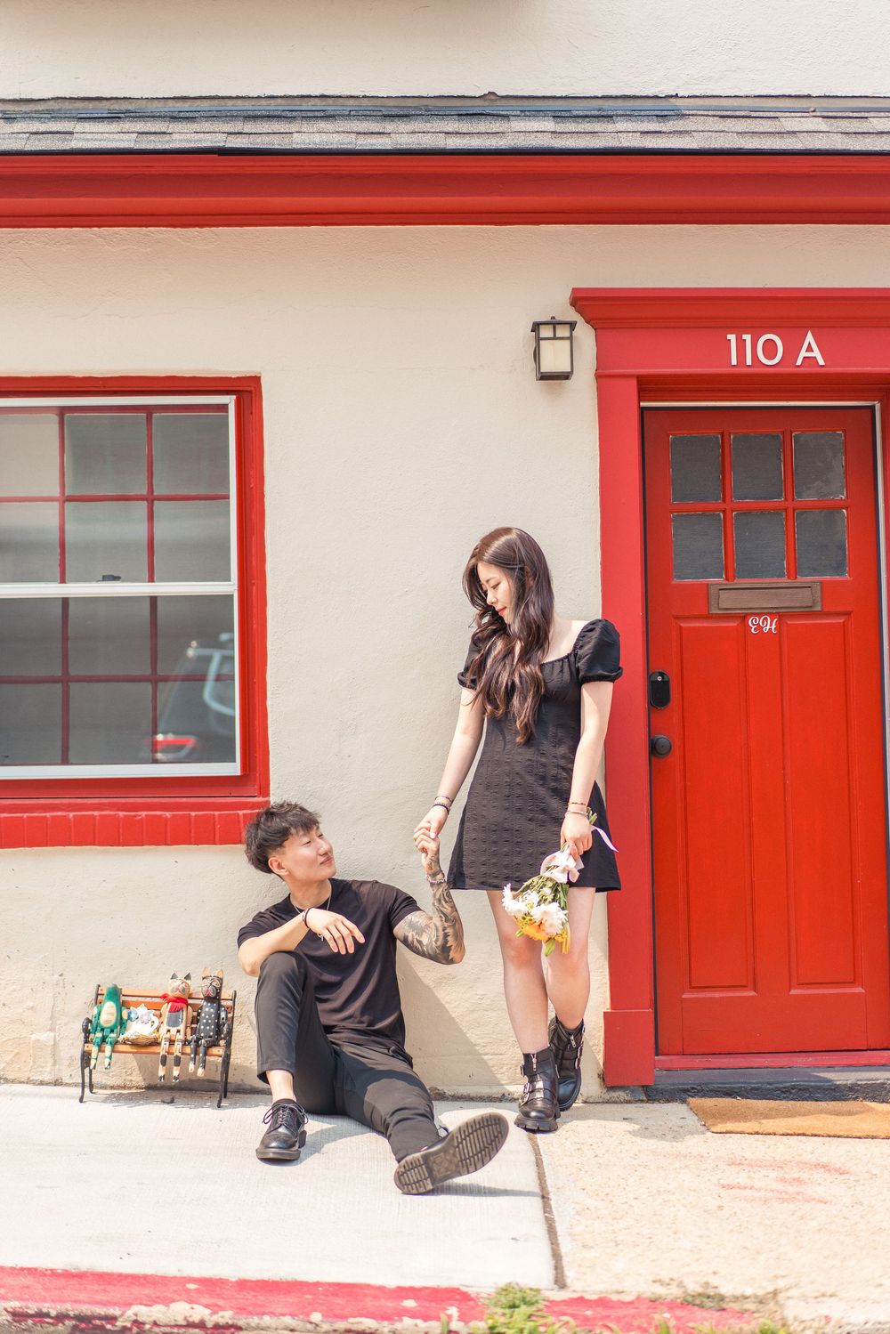 Couple poses playfully outside building with red door and trim.