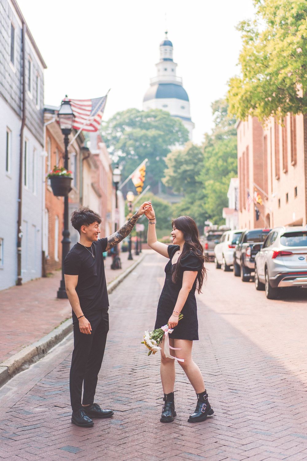 Couple celebrates on cobblestone street with historic state capitol dome visible.