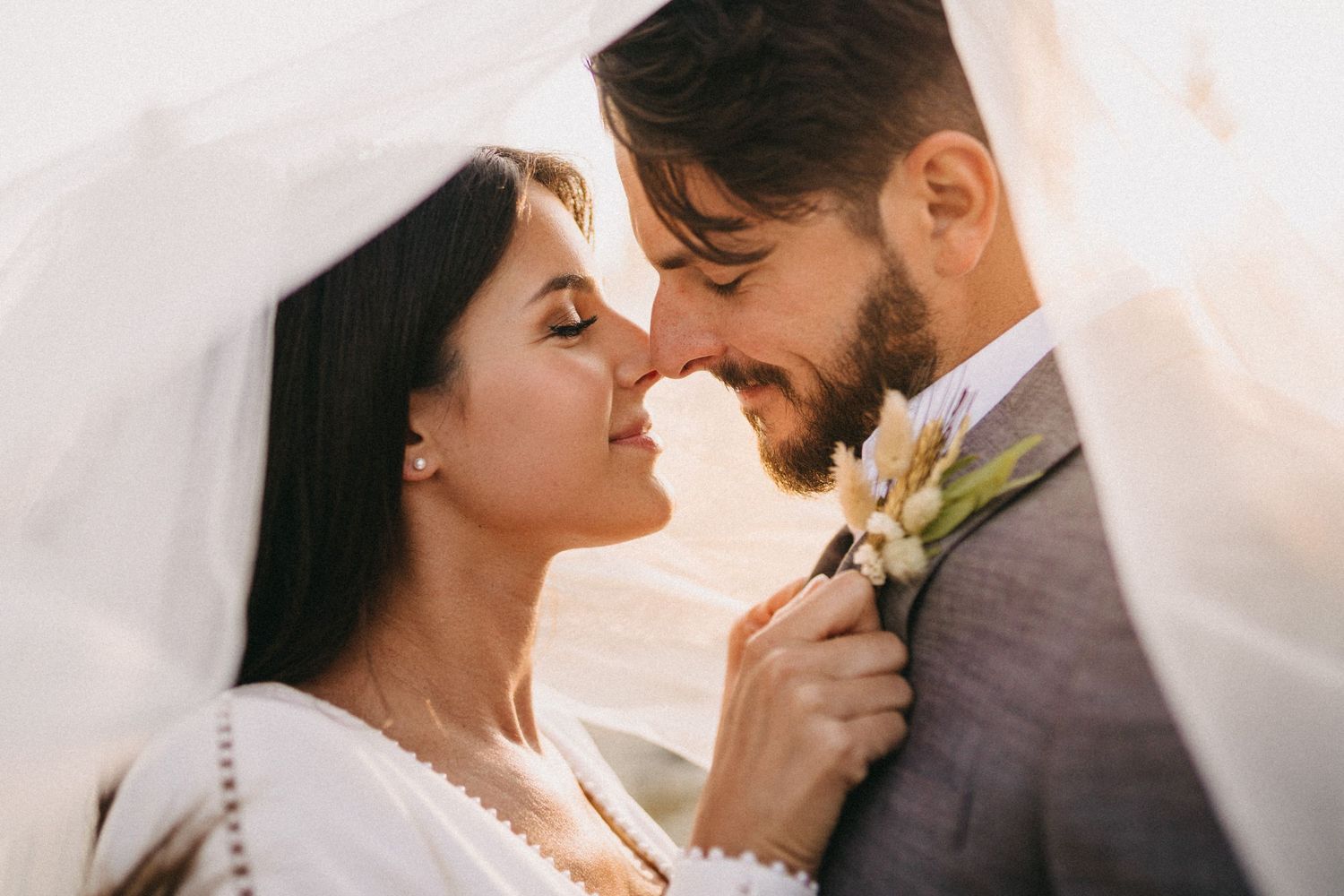 A romantic close-up of newlyweds sharing an intimate moment under a veil during their sunset wedding ceremony.
