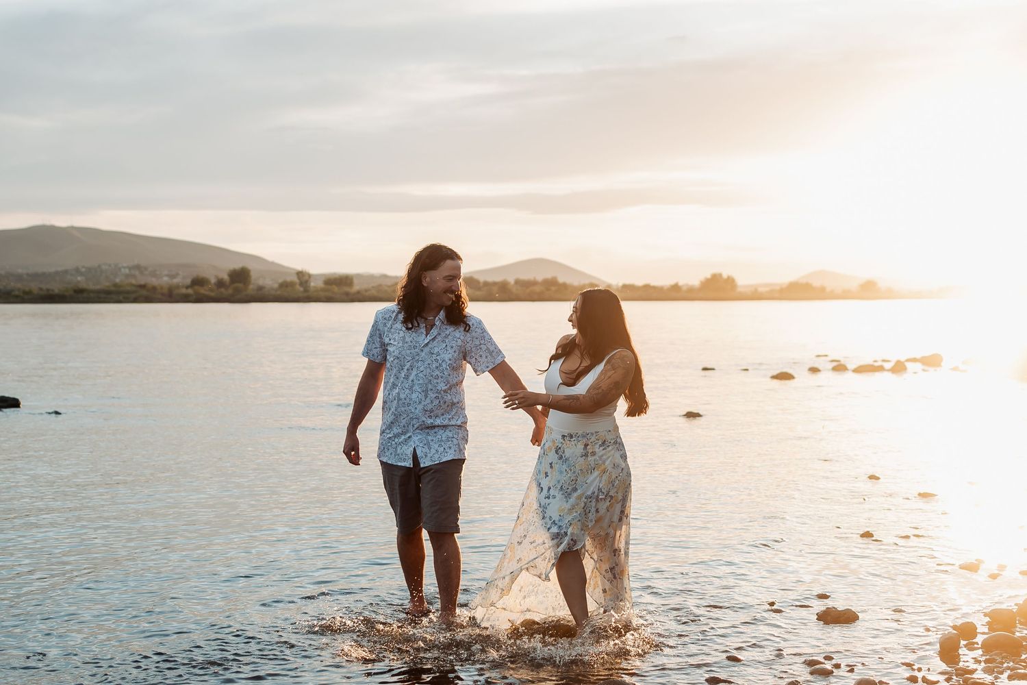 An engaged couple splash together in shallow water at sunset in the Columbia River in Pasco, Washington.