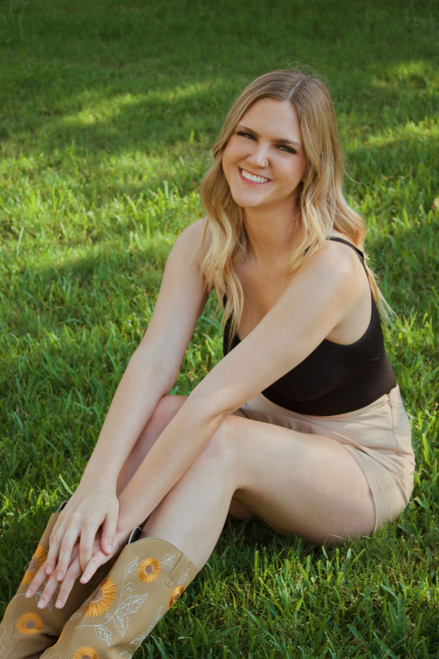 A woman in athletic wear lies in green grass while smiling and stretching during golden hour sunlight.