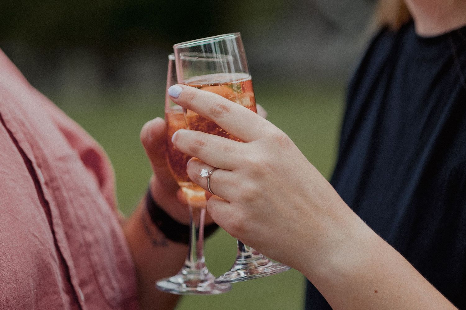 Close-up of two people clinking champagne flutes filled with rose sparkling wine outdoors.