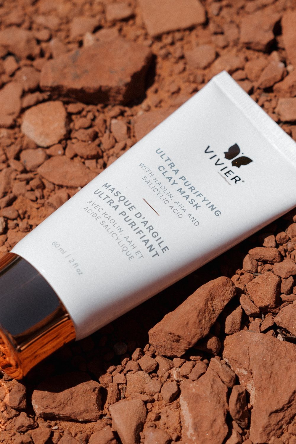 White cosmetic skincare tube from Vitier brand lying on reddish-brown soil or crushed powder background.