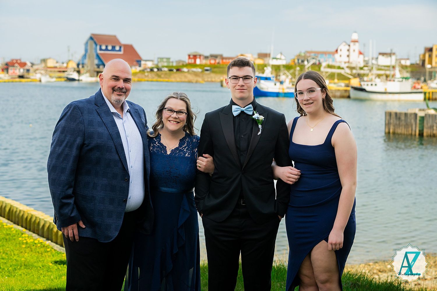 A group poses for a formal photo by the waterfront with boats and coastal buildings in the background.