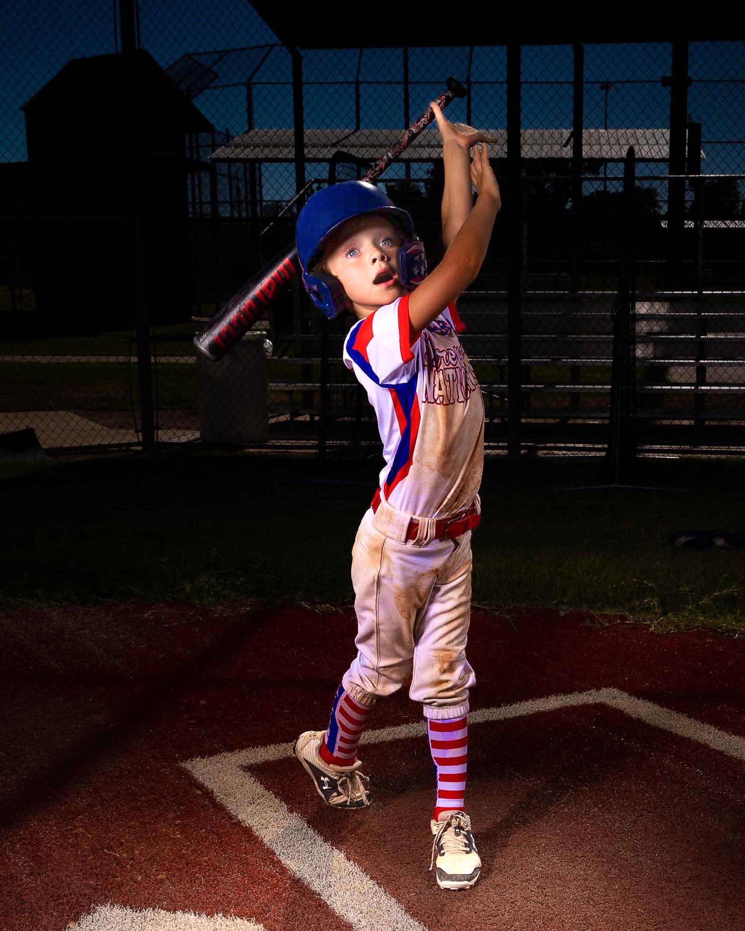 Young baseball player in uniform takes a dramatic batting stance at home plate during evening practice.
