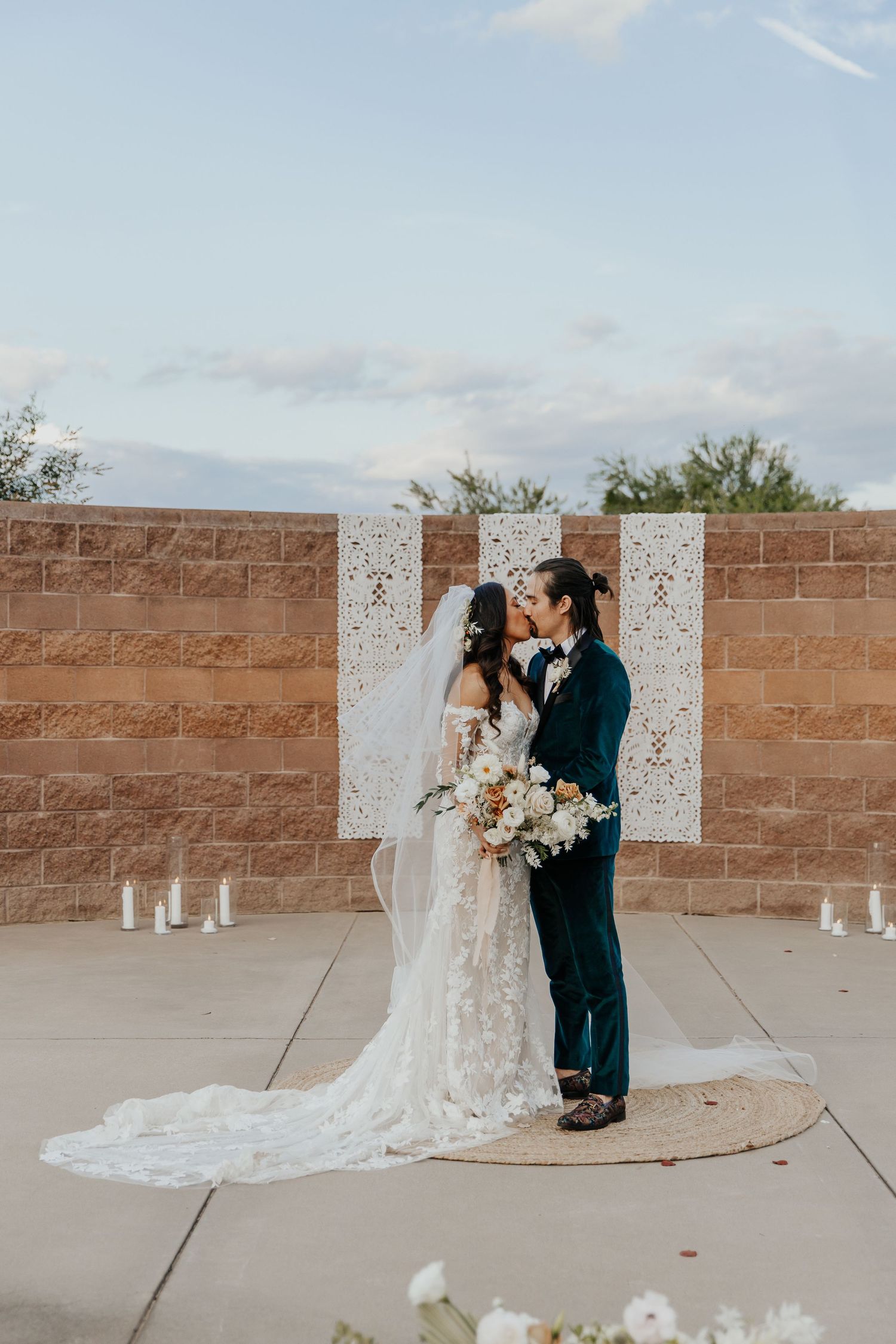 A couple shares an intimate moment in front of a brick wall with white decorative backdrop and candles during their wedding ceremony.