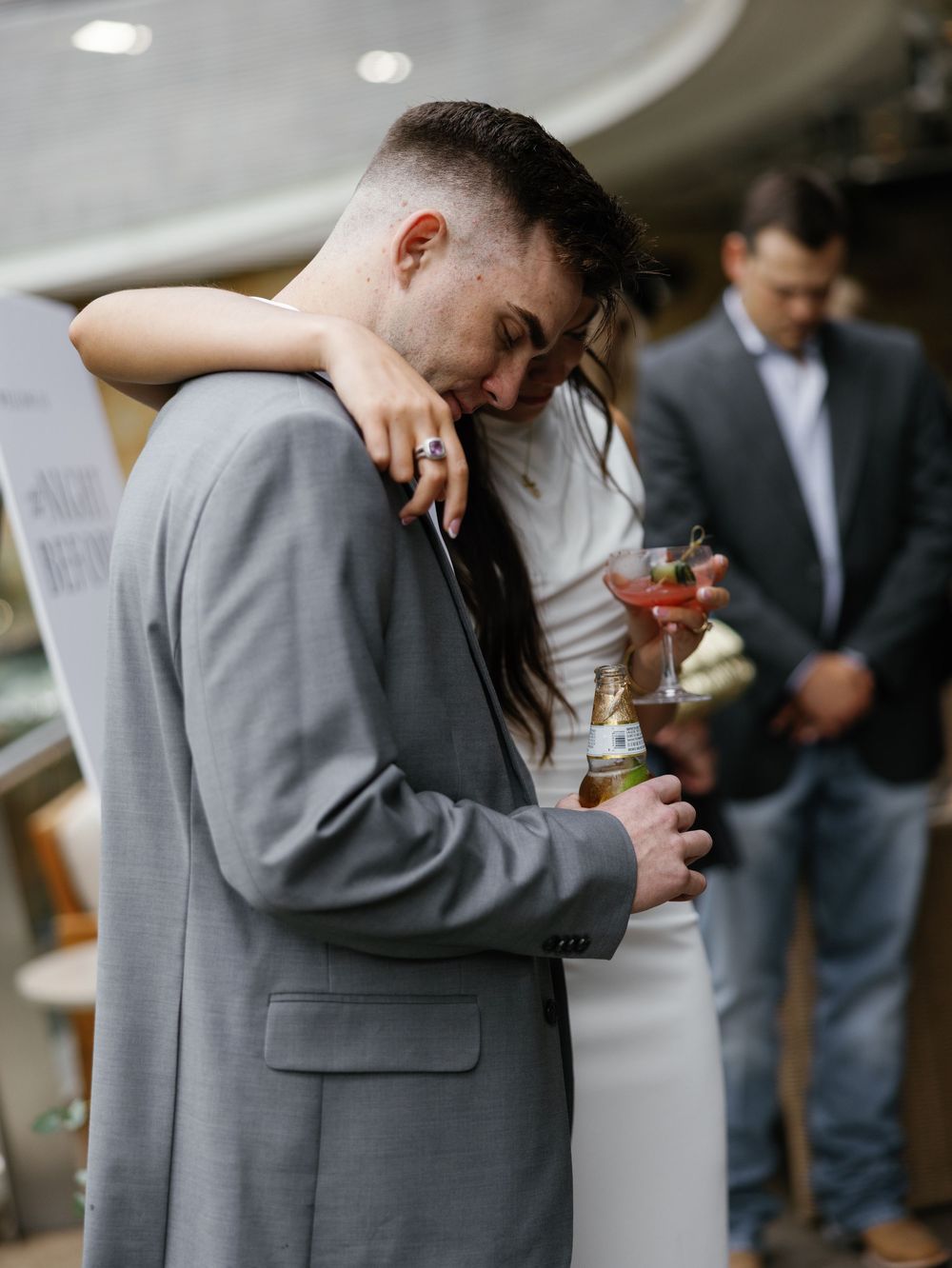 Wedding party members in gray suits sharing drinks and intimate moments at reception.