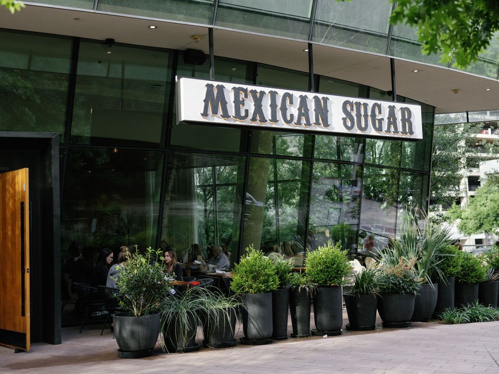 Storefront of Mexican Sugar restaurant with potted plants and modern signage.