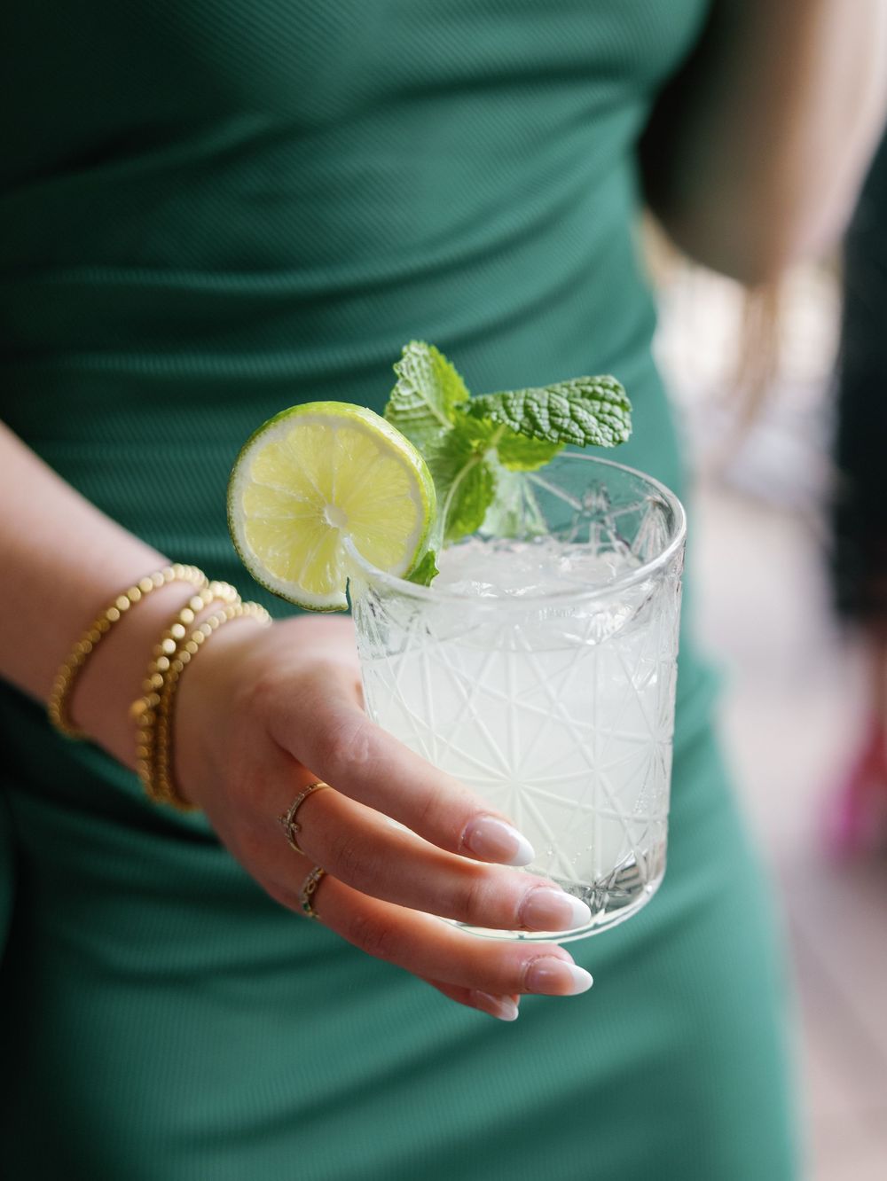 Close-up shots of cocktail glasses with lime garnish and ice being held in emerald green.