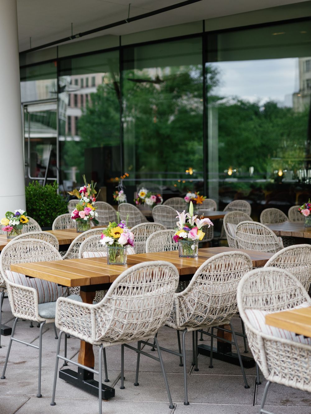 Modern outdoor patio setup with woven chairs and wooden tables for wedding reception.