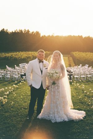 A wedding couple stands in front of empty chairs during golden hour in an outdoor ceremony setting.