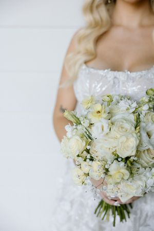 Elegant white bridal bouquet with roses and mixed flowers held against a lace wedding dress.