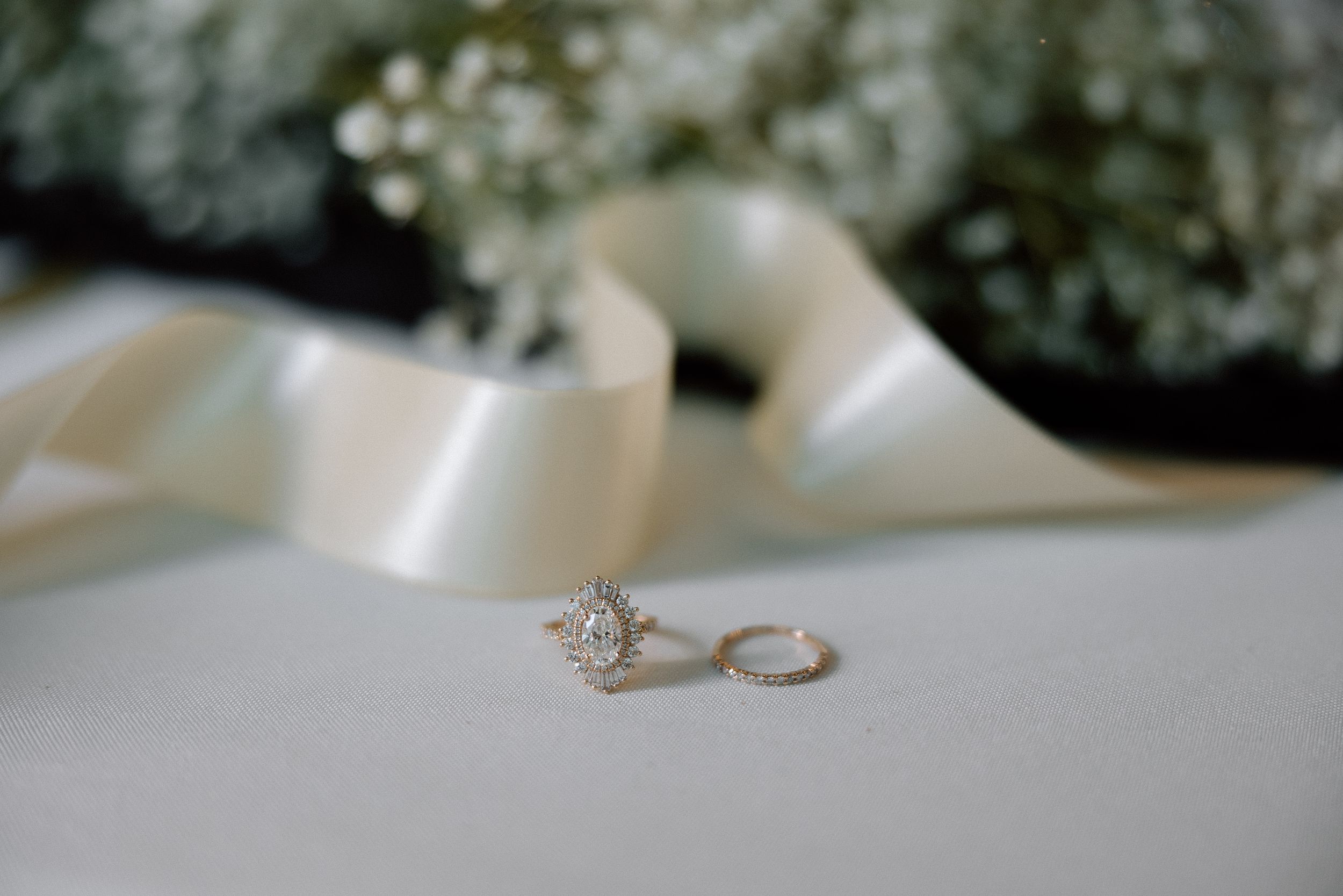Elegant diamond engagement ring and wedding band displayed with white ribbon on light surface.
