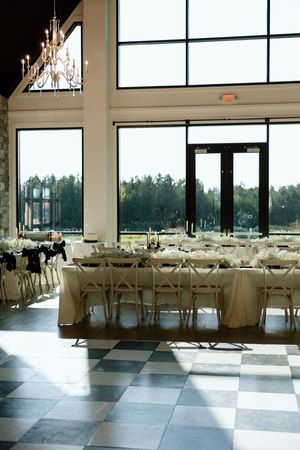 Modern wedding reception venue with checkerboard floor and white table settings under crystal chandeliers.