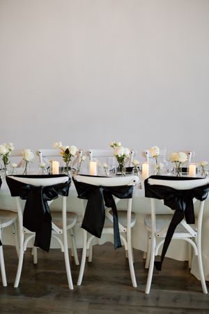 Elegant wedding reception tables with white chairs, black bows, and simple floral centerpieces.