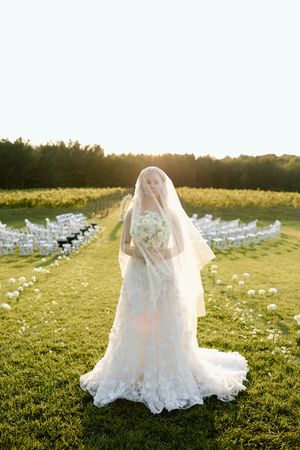 Wedding venue setup outdoors with white chairs and sunset view across an open field.