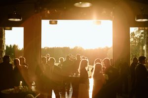 Wedding reception silhouettes against golden sunset streaming through large venue windows.