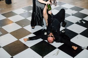 Person lying dramatically on black and white checkered floor at formal event.