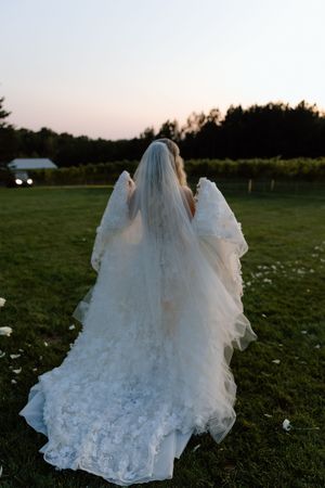 Dramatic back view of flowing lace wedding dress and veil against sunset countryside.