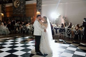 Newlyweds share their first dance on a black and white checkered ballroom floor.