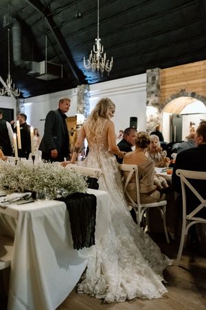 Elegant lace wedding dress with long train shown during reception under vintage chandeliers.